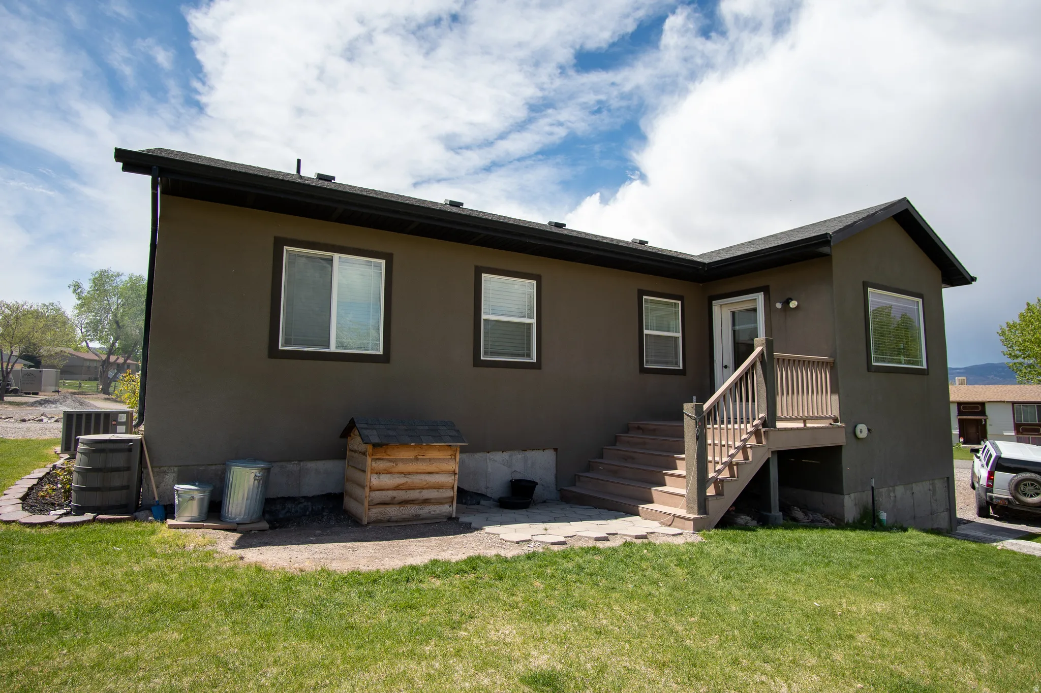 Rear exterior featuring dark stucco siding, white-framed windows, and a black shingle roof