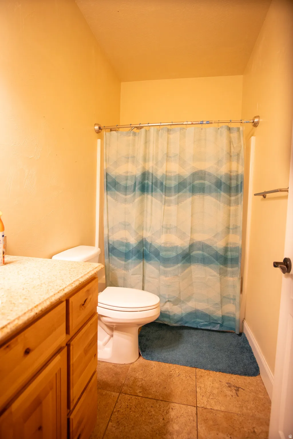 Bathroom with a shower/tub combination, a white toilet, and a vanity featuring wood-finish cabinetry and a light-toned countertop