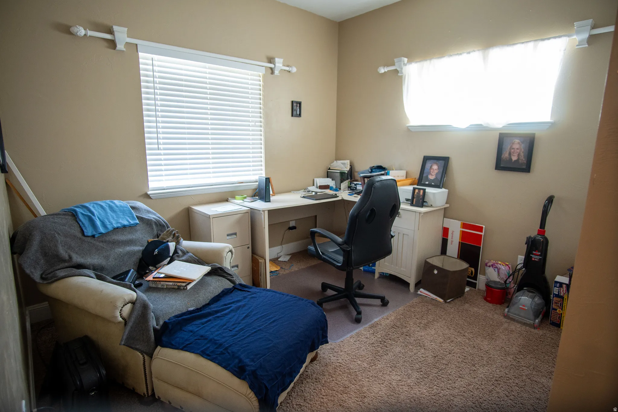 Room featuring two windows with white blinds, neutral-toned walls, and a textured carpet
