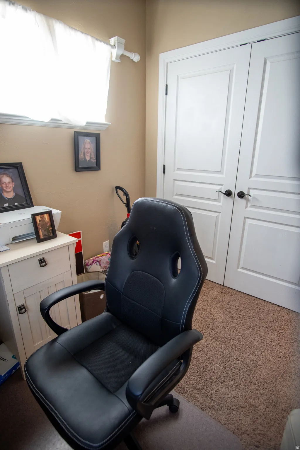 Carpeted room featuring a window with white sheer curtains, a light beige wall color, and white bi-fold doors with black hardware