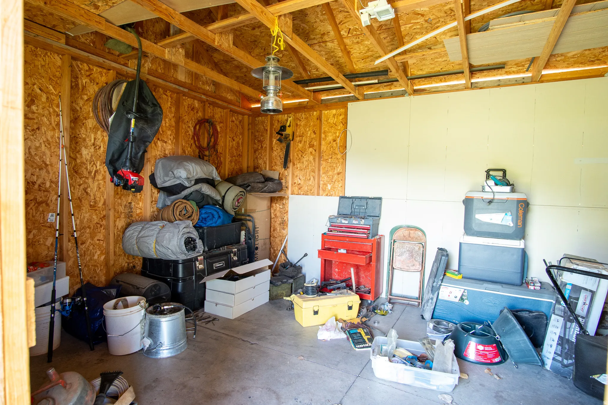 Utility shed interior featuring exposed wood framing, oriented strand board walls, partially finished drywall, concrete flooring, and an exposed rafter ceiling