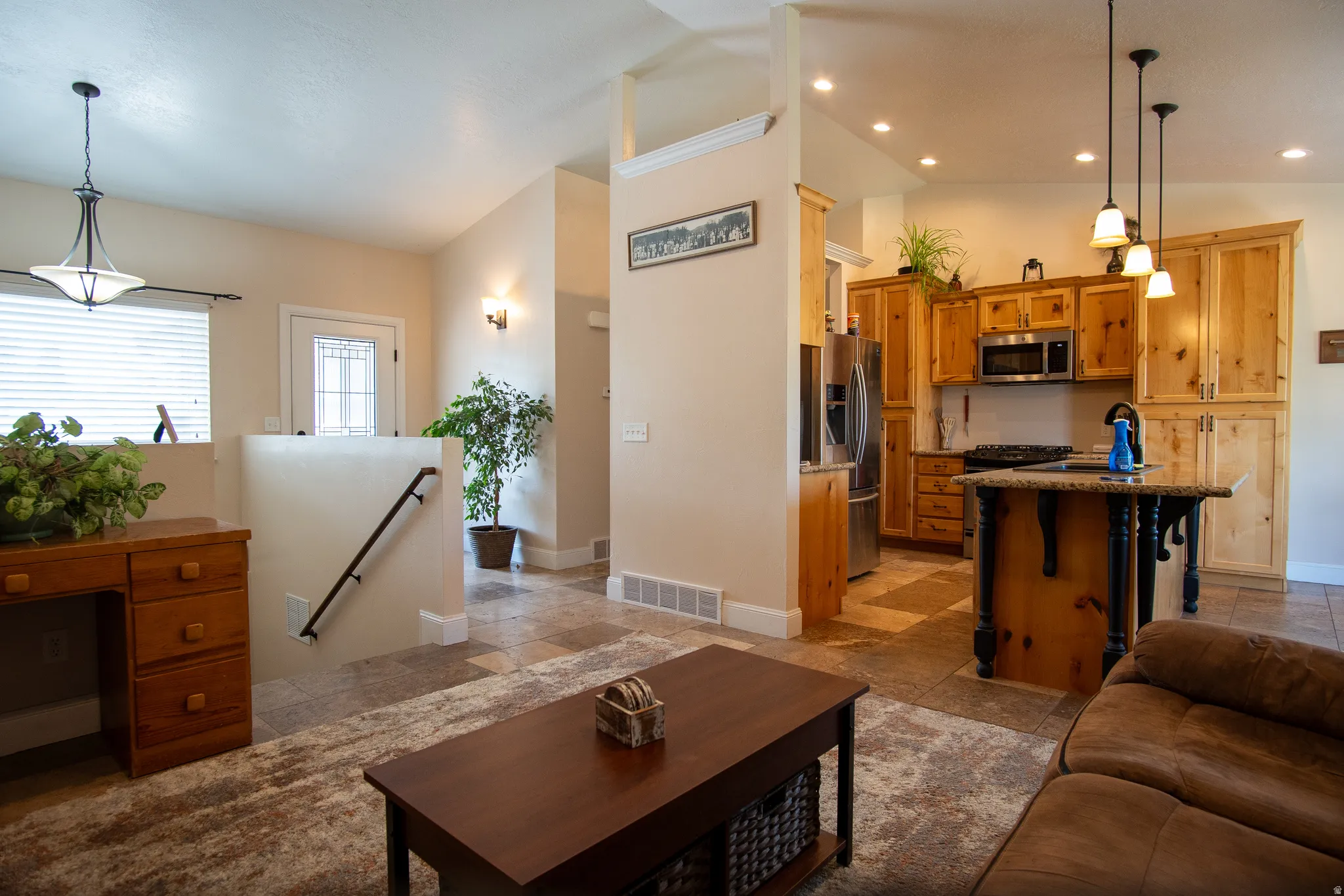 Kitchen featuring wood cabinetry, stainless steel appliances, a center island with a granite-style countertop, and pendant lighting