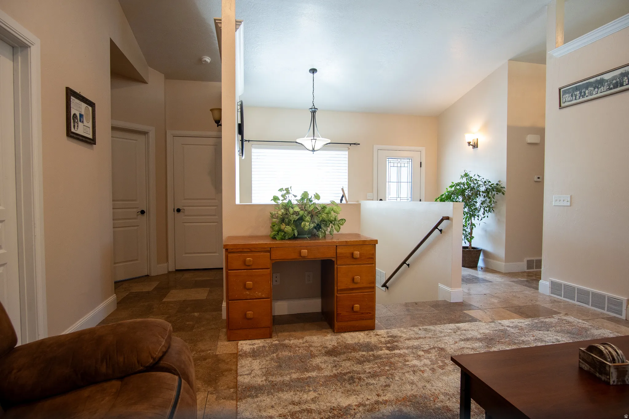Spacious entryway featuring varied tile flooring, a half-wall with a dark wood handrail, and a decorative pendant light fixture