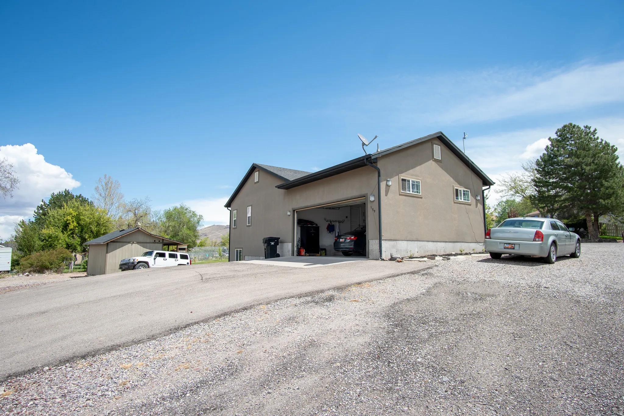 Attached garage with an open bay, gravel driveway, and a separate storage shed