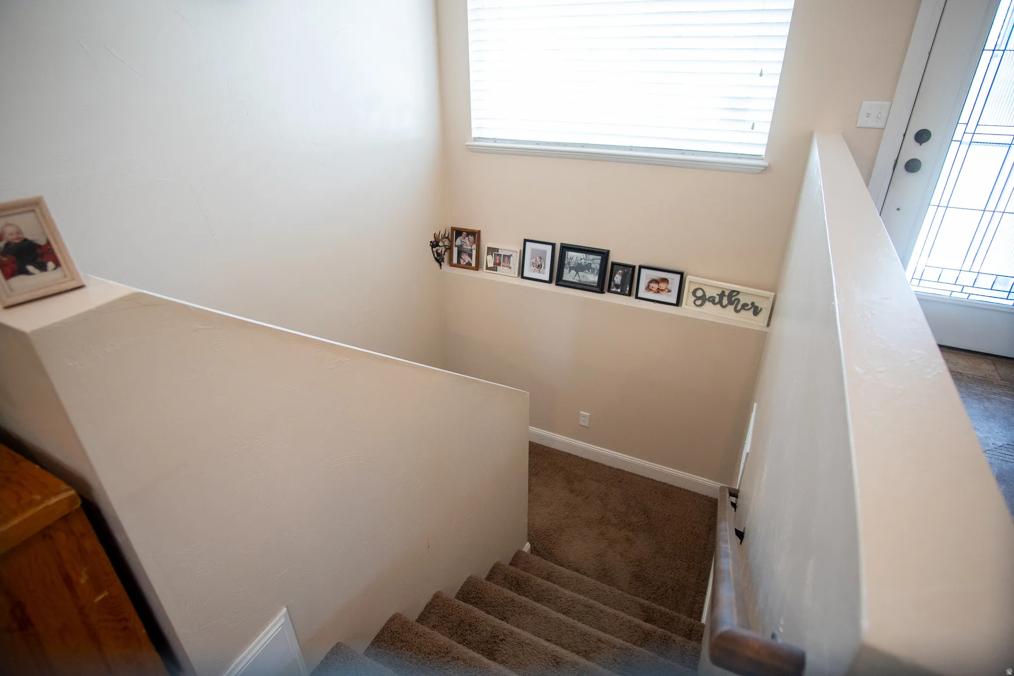 Carpeted staircase with a wood handrail, light beige walls, and a large window with horizontal blinds