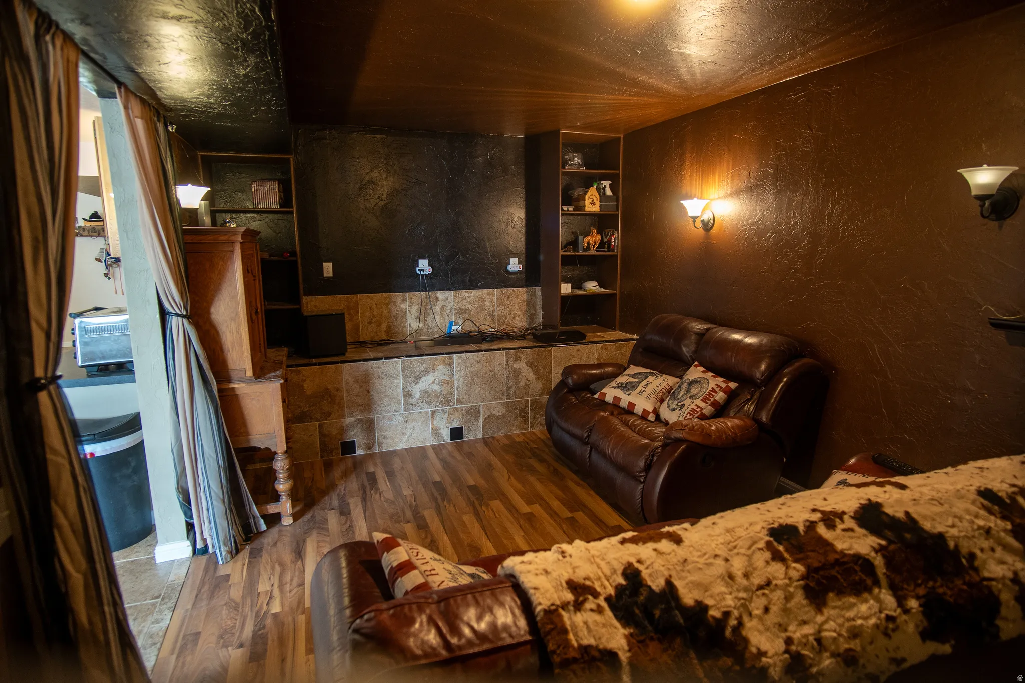 Entertainment area featuring wood-finish flooring, built-in shelving, sconce lighting, and a stone-tiled half-wall