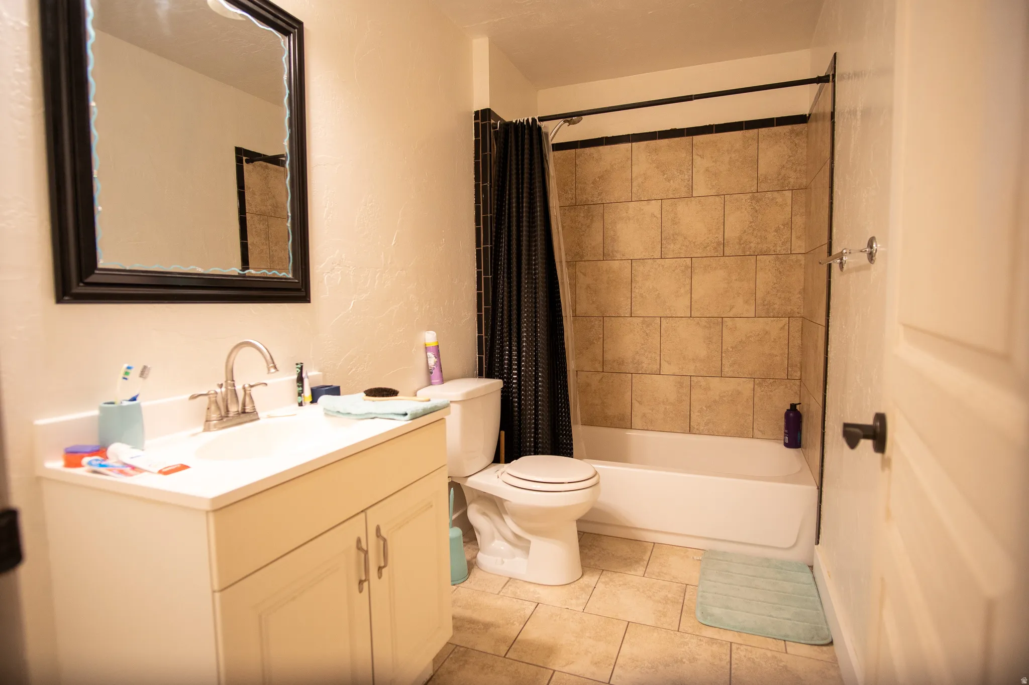 Bathroom featuring a single vanity with a white countertop and base cabinetry, a framed wall mirror, a toilet, and a combination bathtub/shower with tiled surround