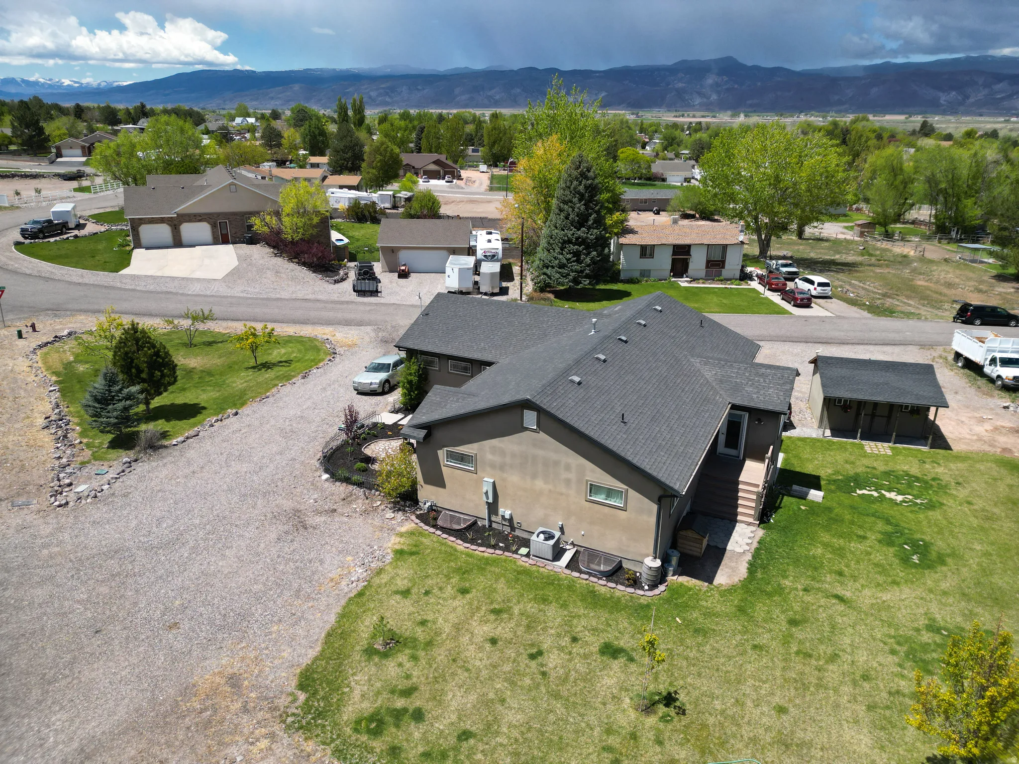Two-story residence featuring a gray asphalt shingle roof, tan stucco siding, and a gravel driveway