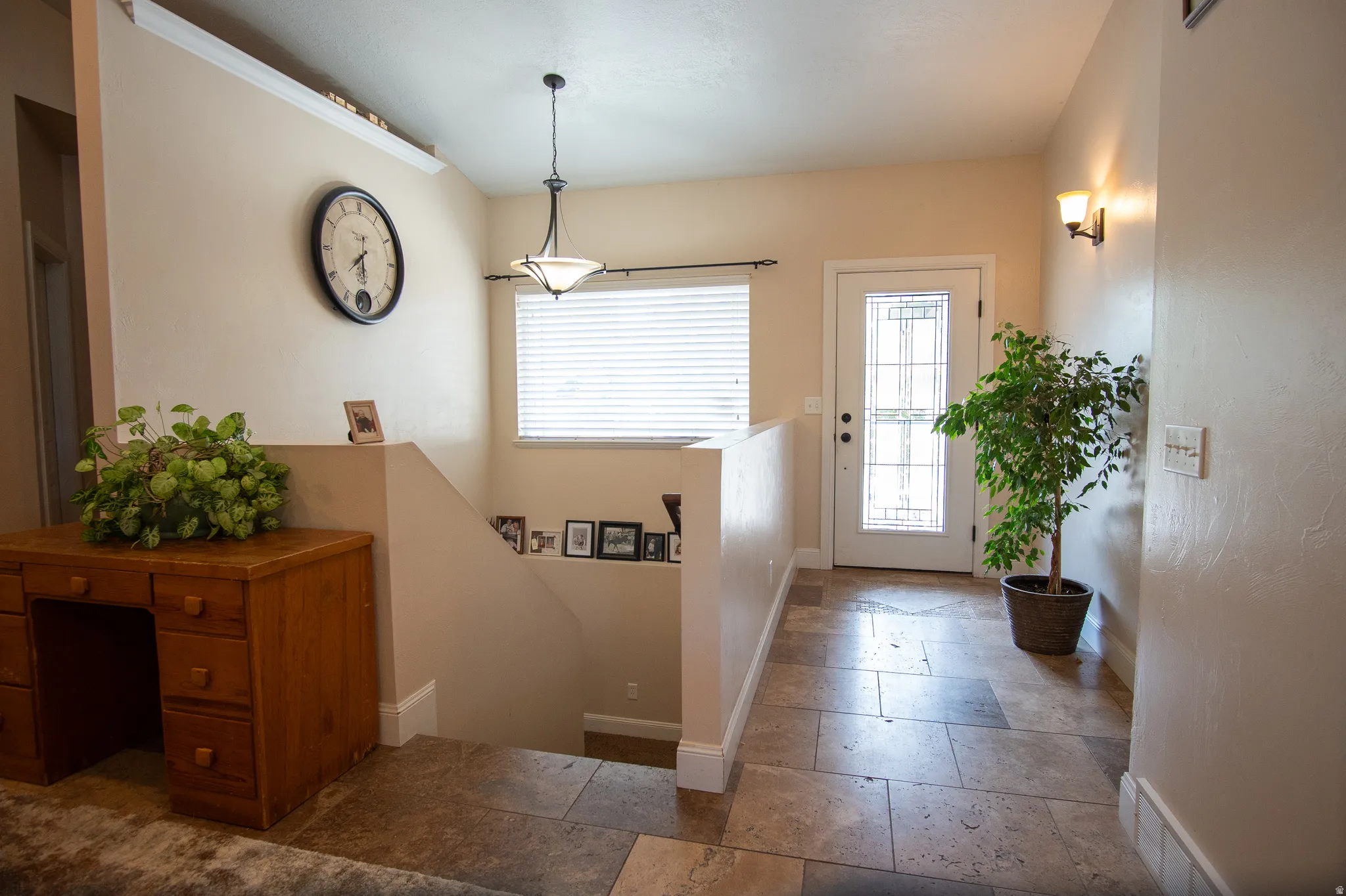 Entryway featuring large format stone tile flooring, a glass-paneled entry door, a contemporary pendant light fixture, and a wall-mounted sconce