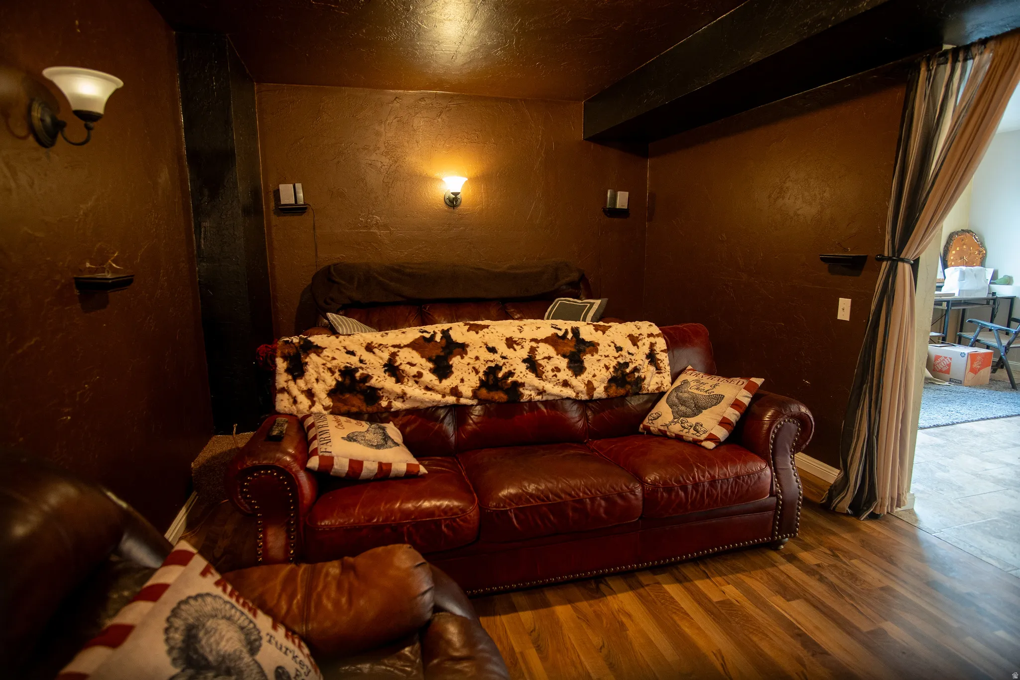 Room featuring wood-finish flooring, a rich brown wall finish, and multiple wall sconces providing ambient lighting