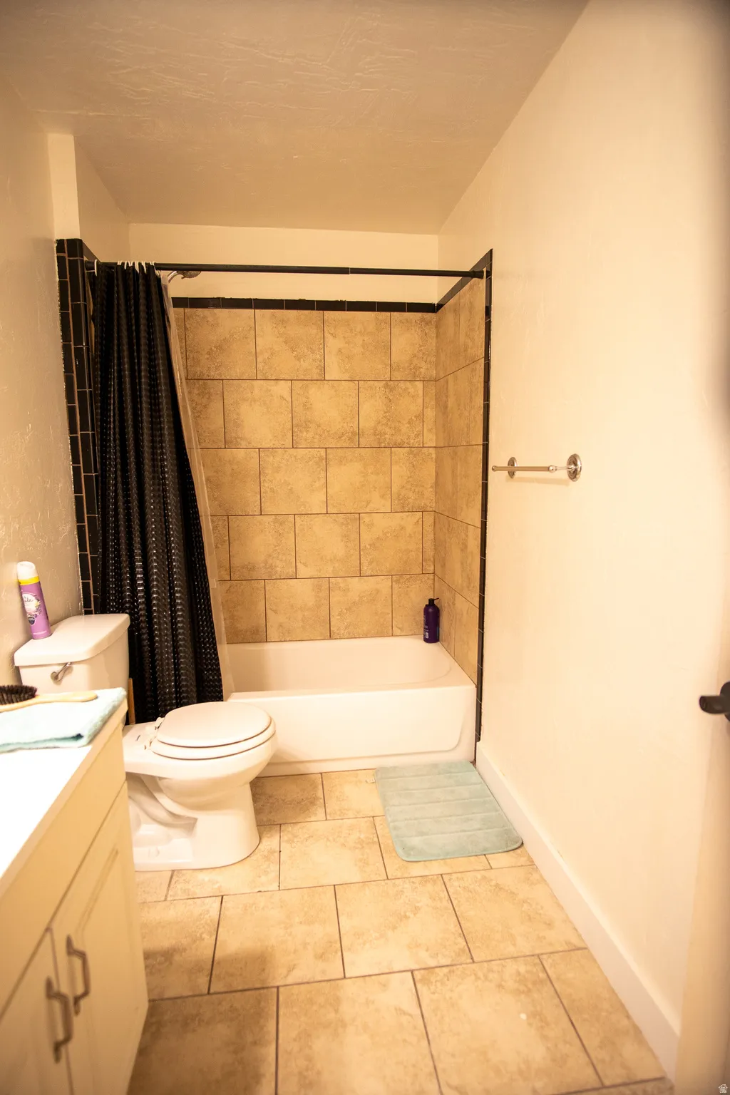 Bathroom featuring a white tub and shower combination with beige tile surround, a white toilet, and a white vanity with storage