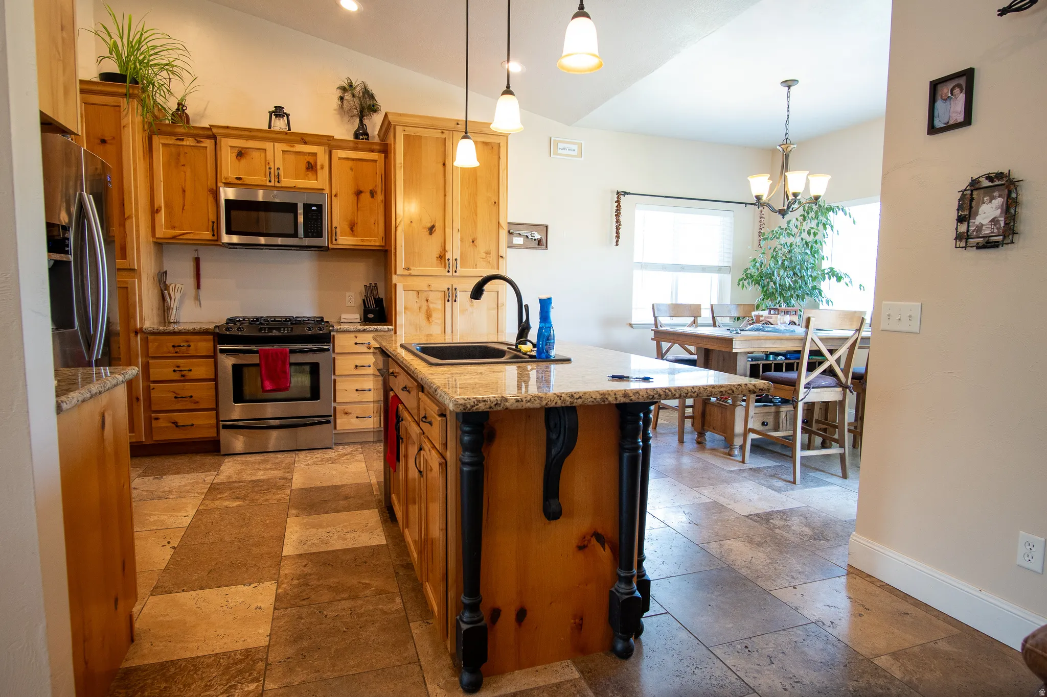 Kitchen featuring wood cabinetry, stainless steel appliances, speckled countertops, and a central island with a black sink