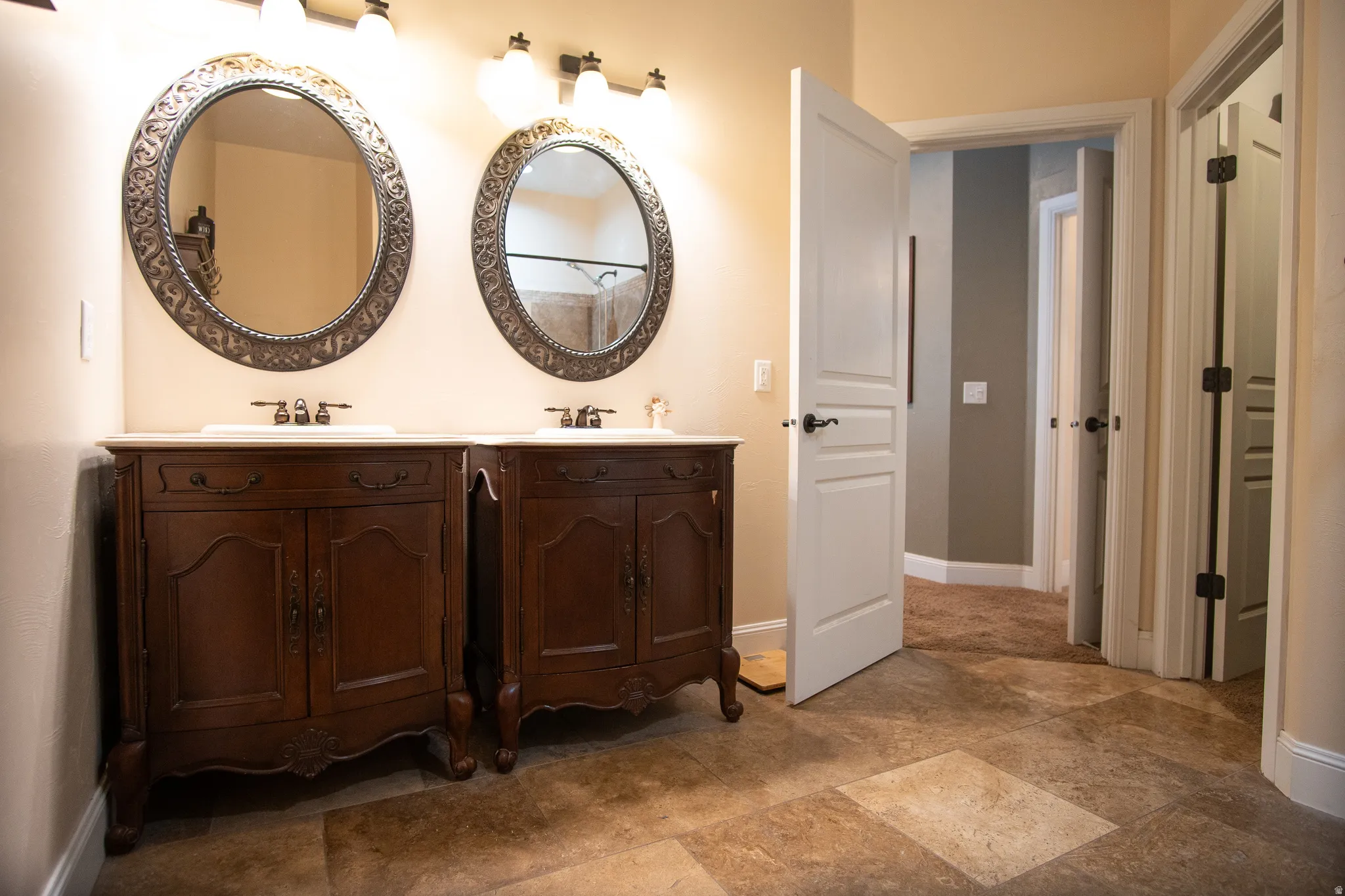 Double vanity featuring individual dark wood base cabinets with white countertops and undermount sinks, bronze faucets, and ornate framed oval mirrors with three-light bronze fixtures