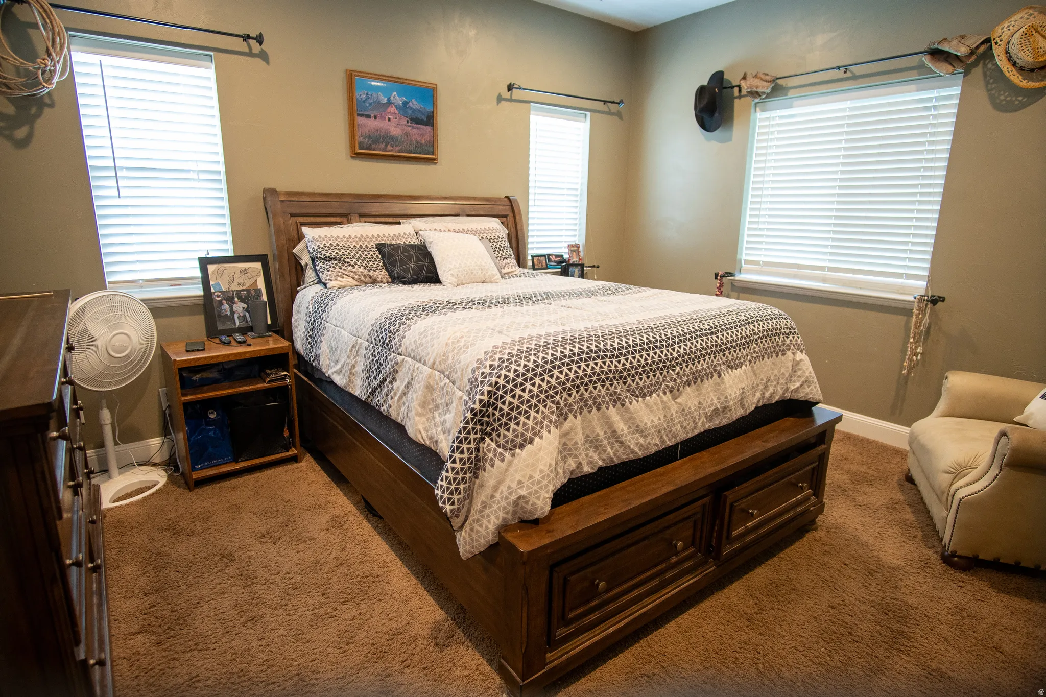 Carpeted room featuring two windows with horizontal blinds, a neutral wall color, and a dark wood-finish bed frame with built-in storage