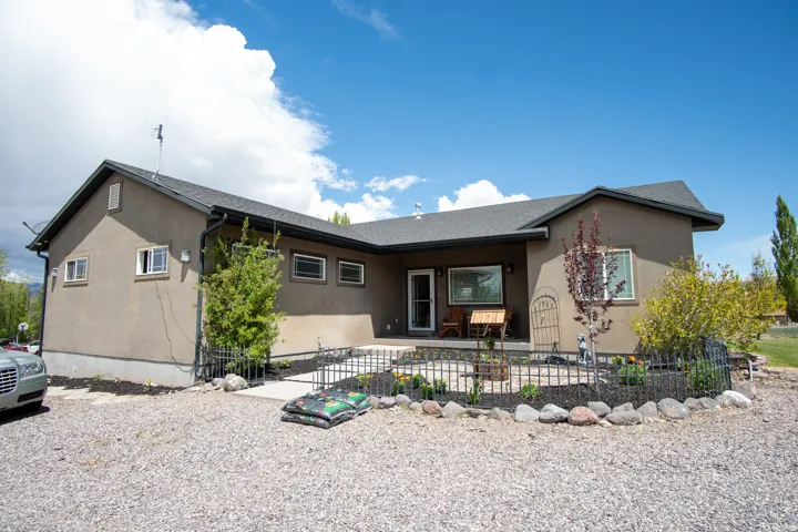 Stucco exterior with a dark shingle roof, featuring a front patio area, decorative metal fencing, and established plantings