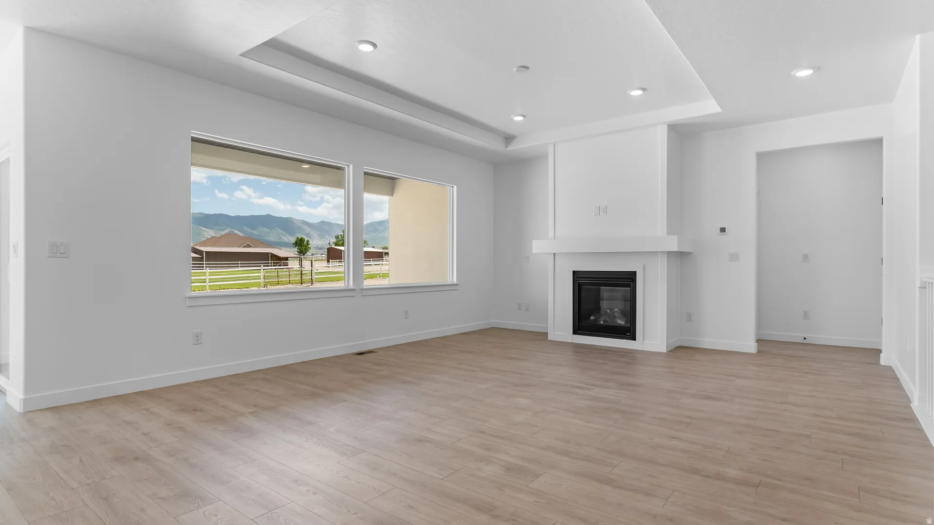 Spacious living area featuring wood-finish flooring, a contemporary fireplace with a white mantel, and recessed lighting