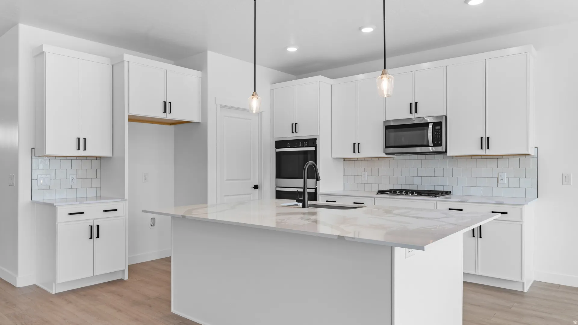 Spacious kitchen featuring an expansive island with a waterfall-edge countertop, white shaker cabinetry, stainless steel appliances, and a subway tile backsplash