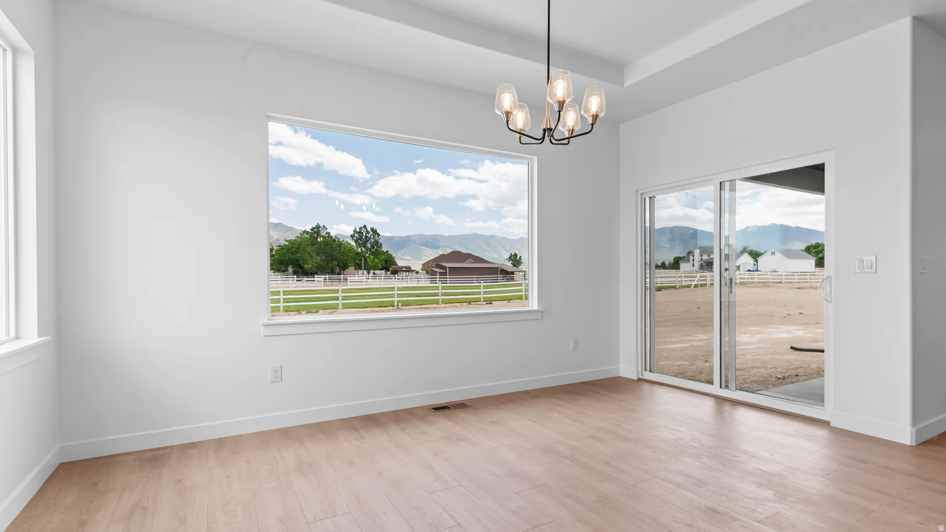 Bright open room featuring wood-finish flooring, a contemporary chandelier, a large picture window, a secondary window, and sliding glass doors