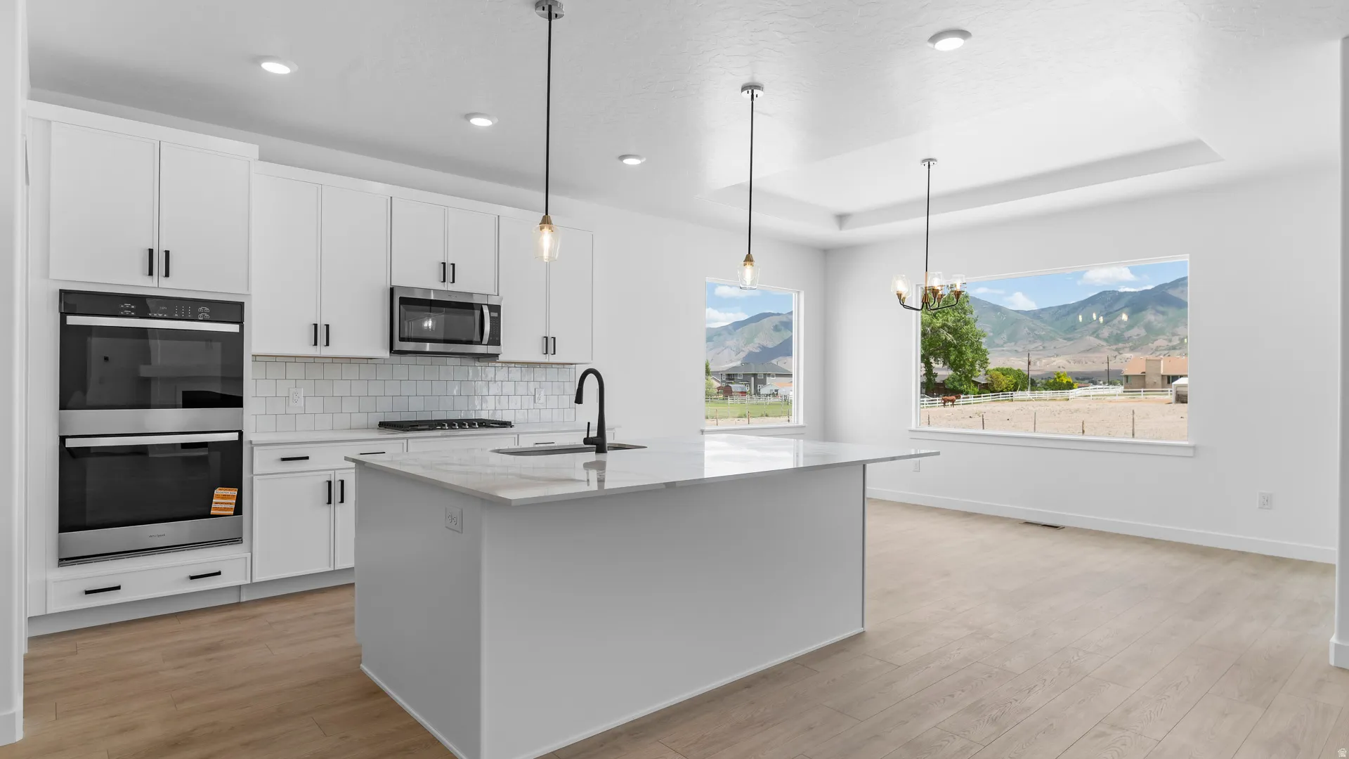 Contemporary kitchen island with a stone countertop, white cabinetry, integrated stainless steel double ovens, and wood-finish flooring
