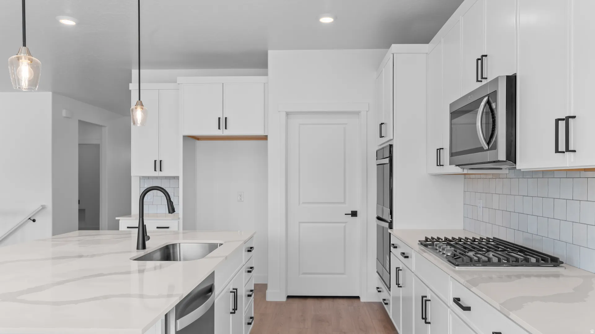 Modern kitchen featuring white cabinetry, a large kitchen island with a built-in sink, stainless steel appliances, and a gas cooktop