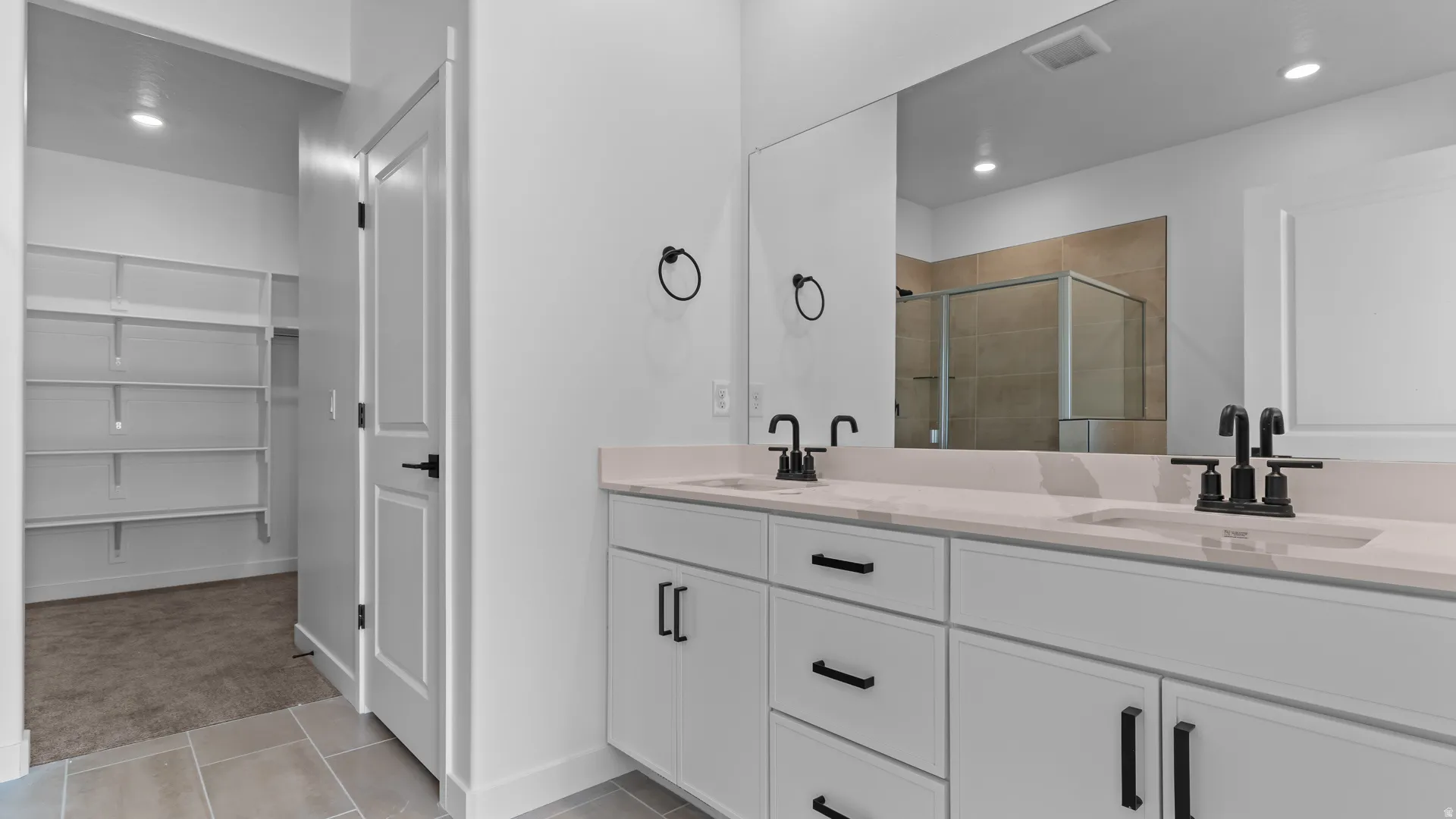 Dual vanity with quartz countertops, integrated sinks, matte black fixtures, and a frameless mirror