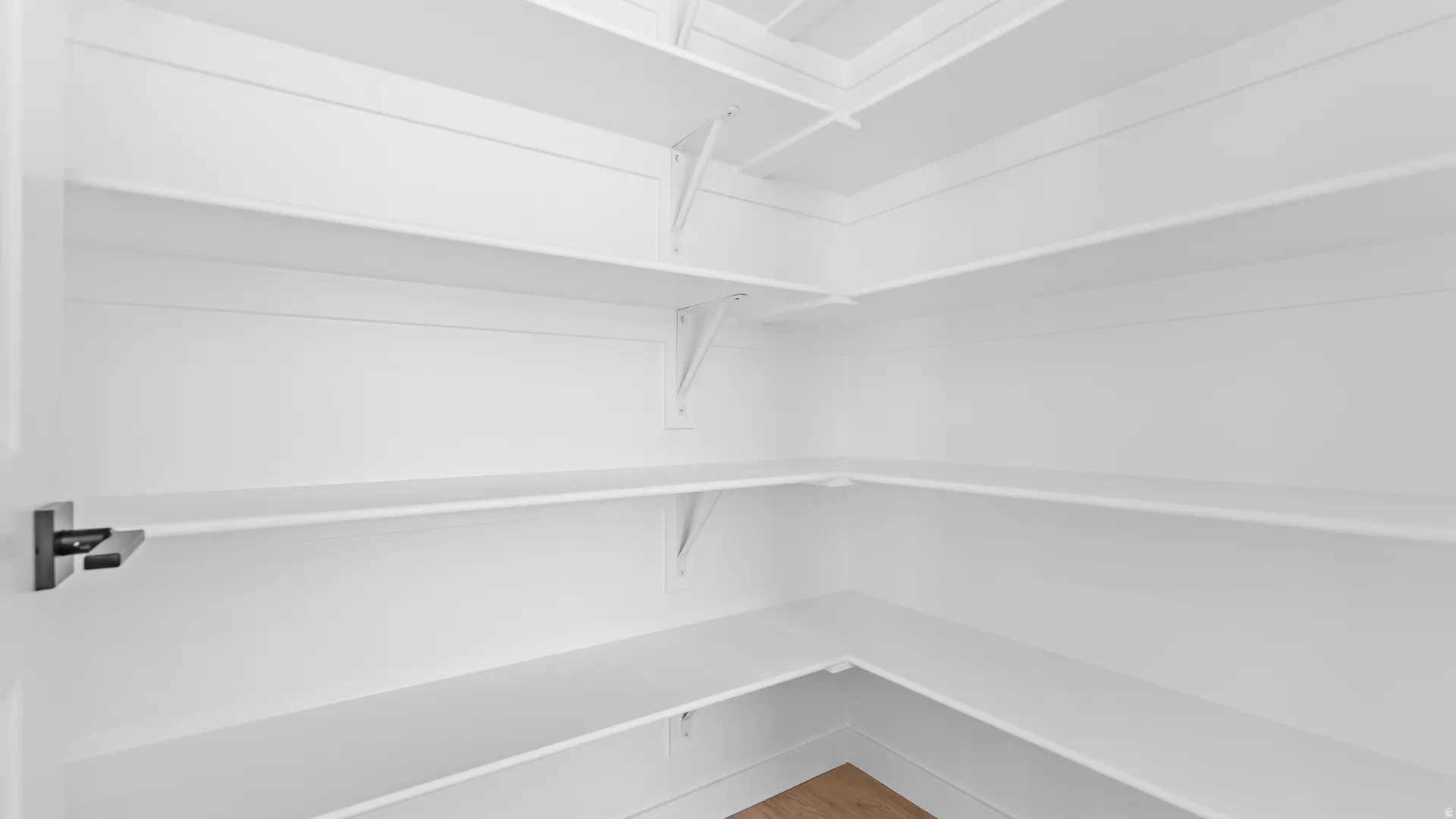 Walk-in pantry with extensive white shelving, a light wood-finish floor, and a black door handle