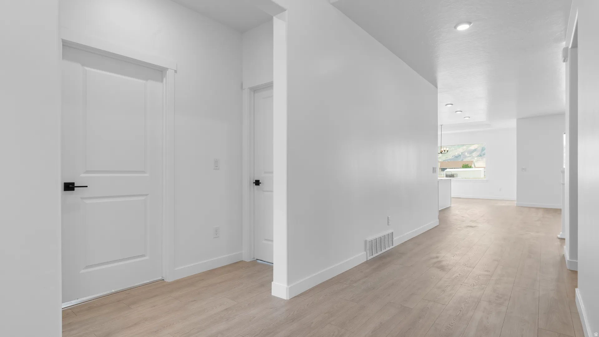 Hallway with light wood-finish flooring, white walls, recessed lighting, and modern white doors with matte black hardware