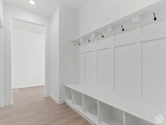 Built-in mudroom bench with integrated cubby storage, board-and-batten wall treatment, matte black hooks, and wood-finish flooring