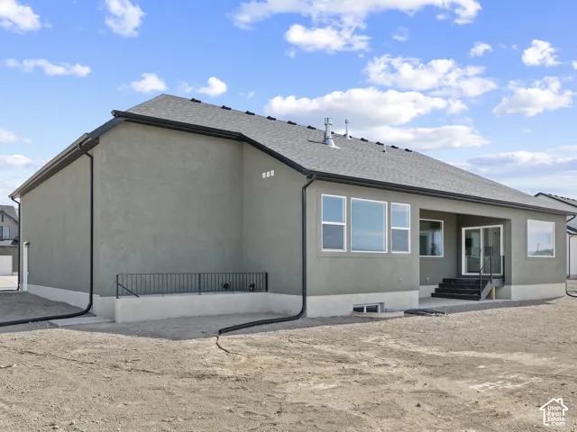 Stucco exterior featuring a dark asphalt shingle roof, black metal railing, concrete foundation, and glass sliding door entry