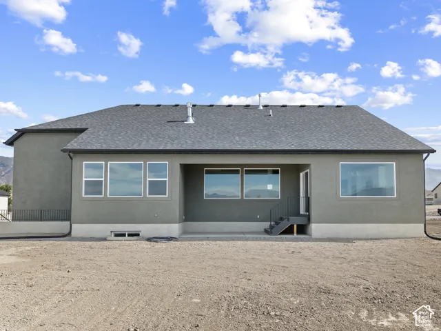 Exterior rear elevation featuring a gray stucco facade, asphalt shingle roof, expansive gridless windows, concrete foundation, and a metal-railed staircase