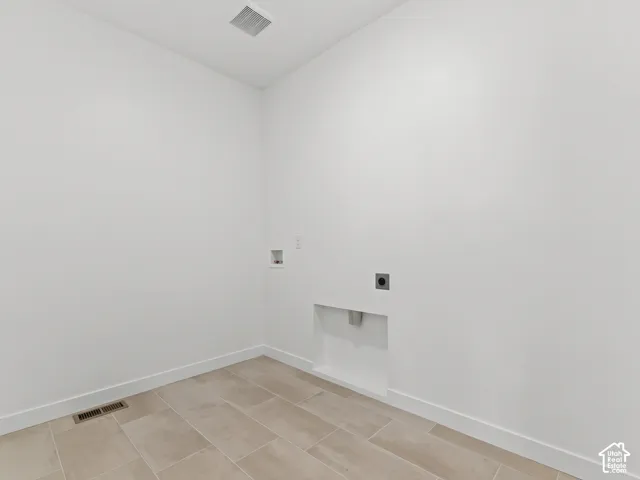Utility room featuring neutral tile flooring, recessed plumbing connections, and a dedicated recessed wall alcove