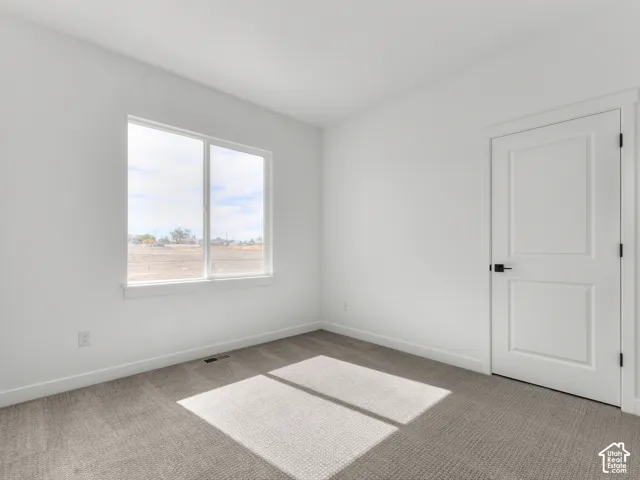 Room interior featuring neutral wall-to-wall carpeting, white walls, a single-pane sliding window, and a white paneled door with matte black hardware