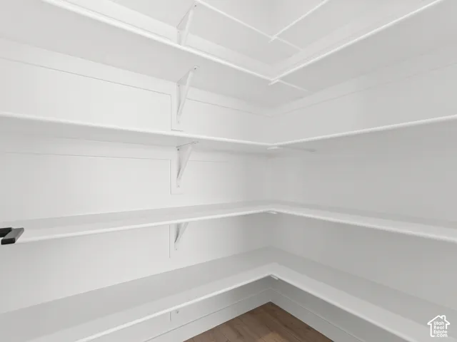 Storage area featuring wrap-around white shelving, vertical wall-mounted support brackets, and wood-finish flooring