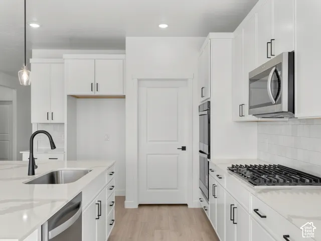 Kitchen featuring white cabinetry with matte black hardware, stone-finish countertops, subway tile backsplash, built-in stainless steel double oven, and wood-finish flooring