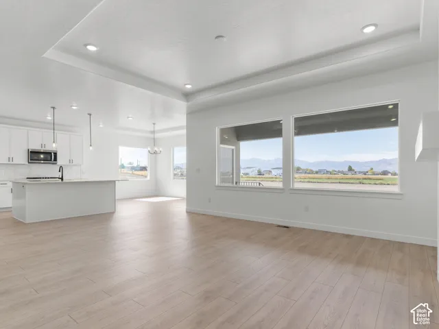 Open-concept interior featuring tray ceilings, wood-finish flooring, recessed lighting, a kitchen island, and large windows capturing mountain scenery