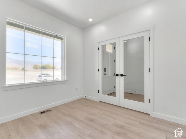 Room featuring wood-finish flooring, recessed lighting, white walls, double French doors with glass panels and matte black hardware, and a large multi-pane window