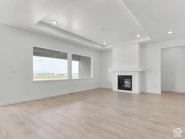 Living area featuring a tray ceiling, recessed lighting, wood-finish flooring, a built-in fireplace with a mantel, and oversized picture windows