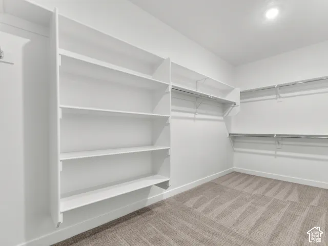 Walk-in closet featuring white built-in shelving, dual-tier metal hanging rods, and carpeted flooring