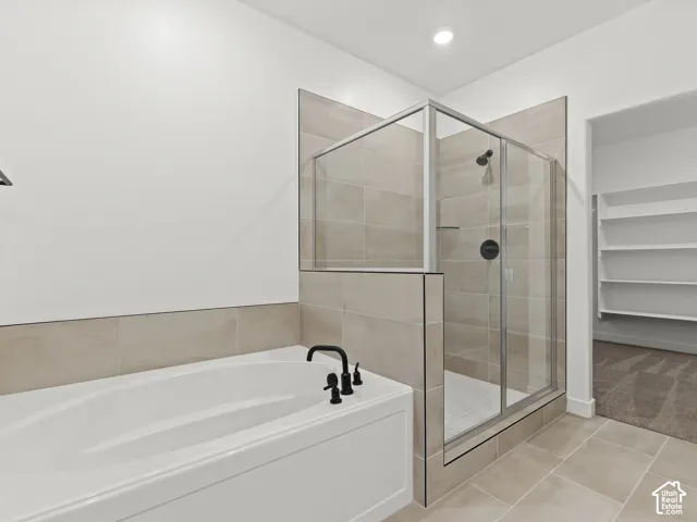 Soaking tub with matte black faucet, walk-in shower with tile surround and glass enclosure, and built-in shelving