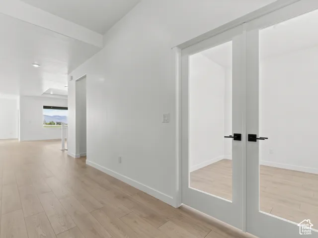 French double doors with glass panels and matte black hardware, paired with light-toned wood-finish flooring throughout the interior