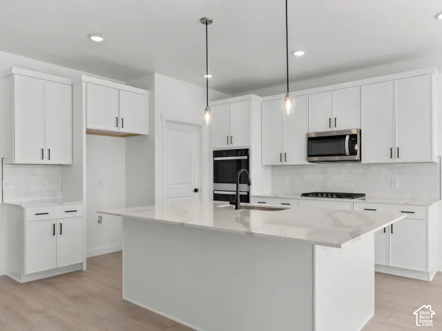 Kitchen featuring white shaker-style cabinetry, quartz countertops with a waterfall edge island, subway tile backsplash, stainless steel built-in double ovens and microwave, and wood-finish flooring
