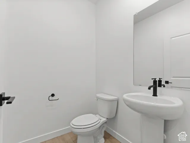 Pedestal sink featuring a matte black faucet, wall-mounted mirror, wood-finish flooring, and matte black hardware