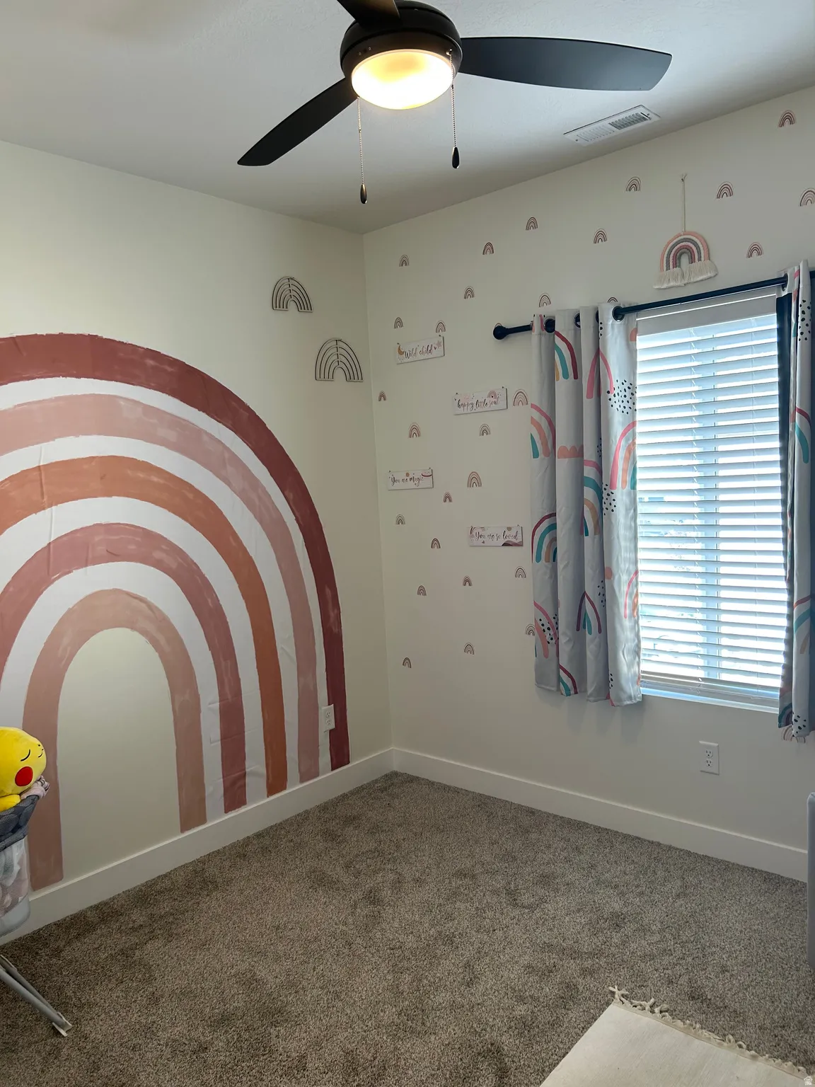 Neutral-toned walls featuring a painted rainbow mural, complemented by a ceiling fan with integrated lighting