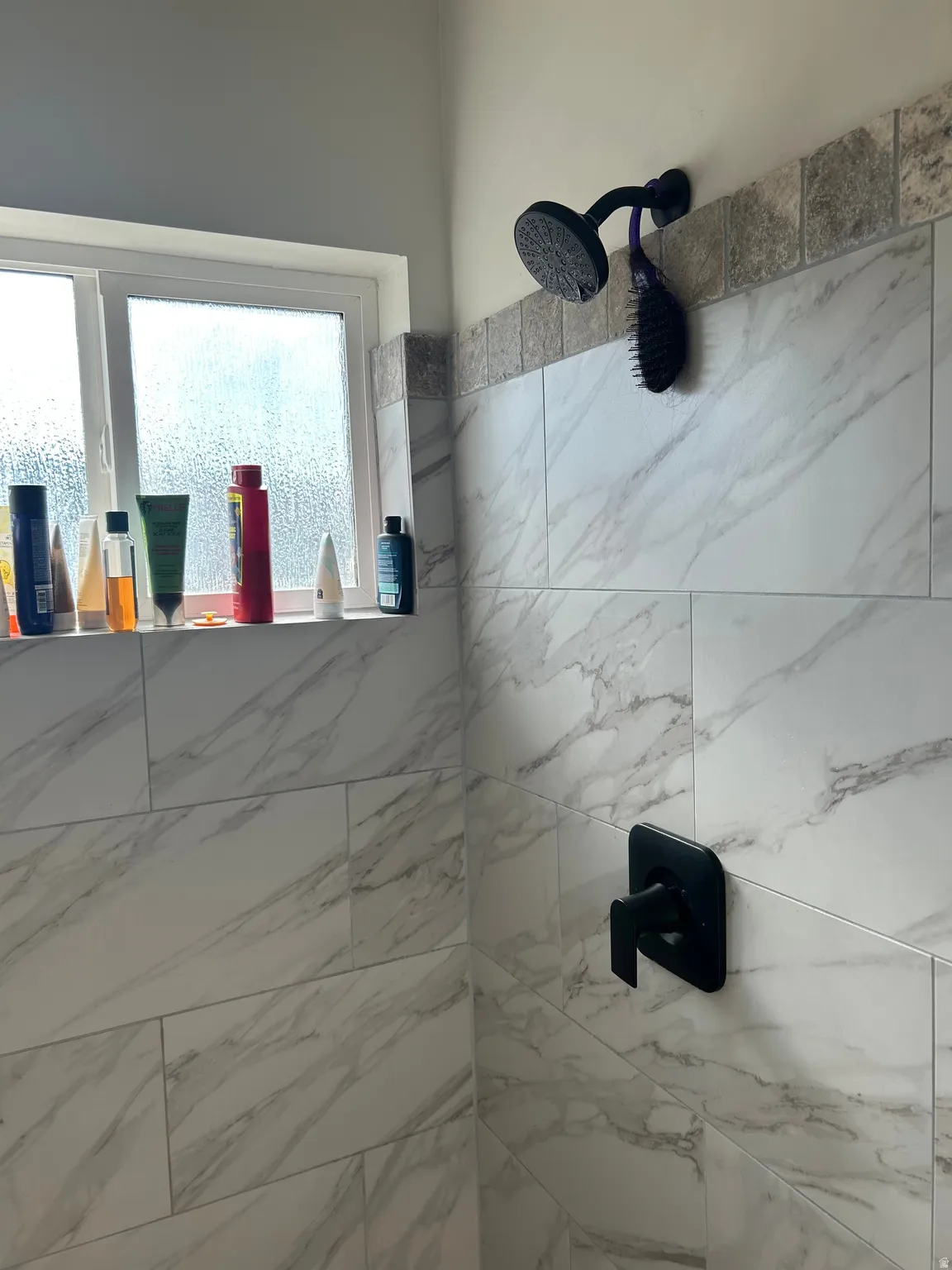 Shower featuring large format marble-look tile, a mosaic tile accent band, and a matte black rainfall showerhead