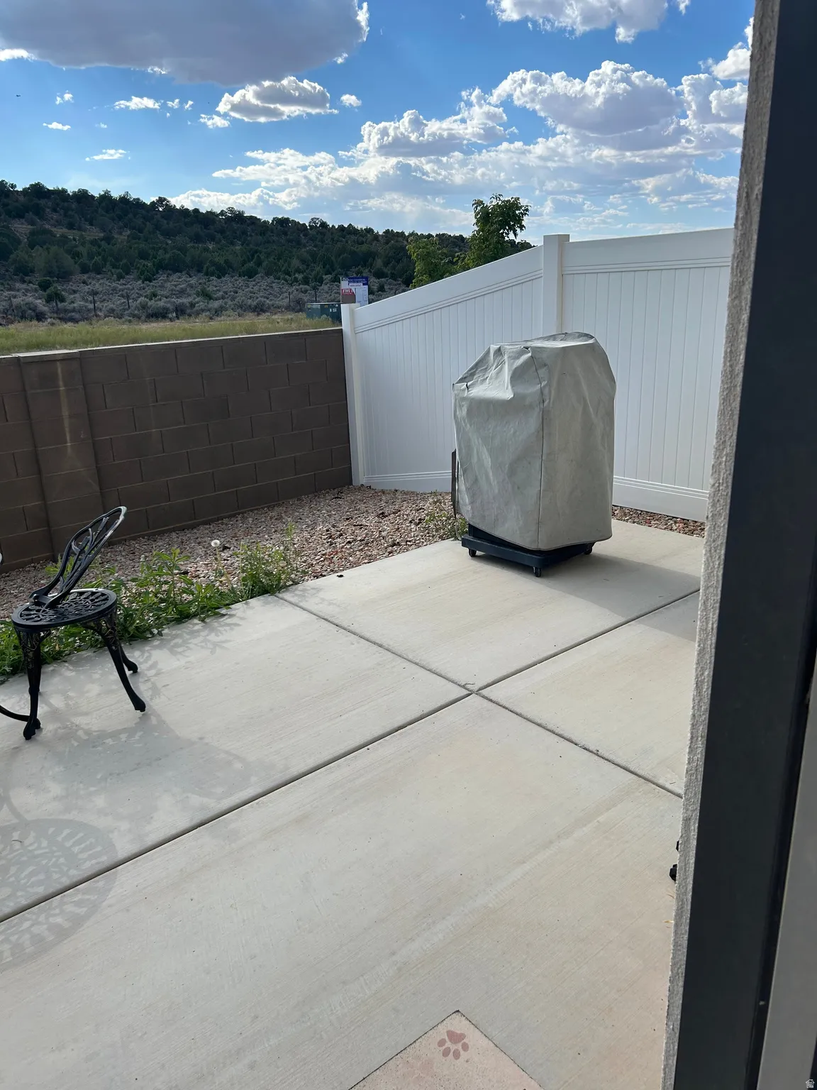 Concrete patio area featuring a block wall, white privacy fencing, and a natural landscape backdrop