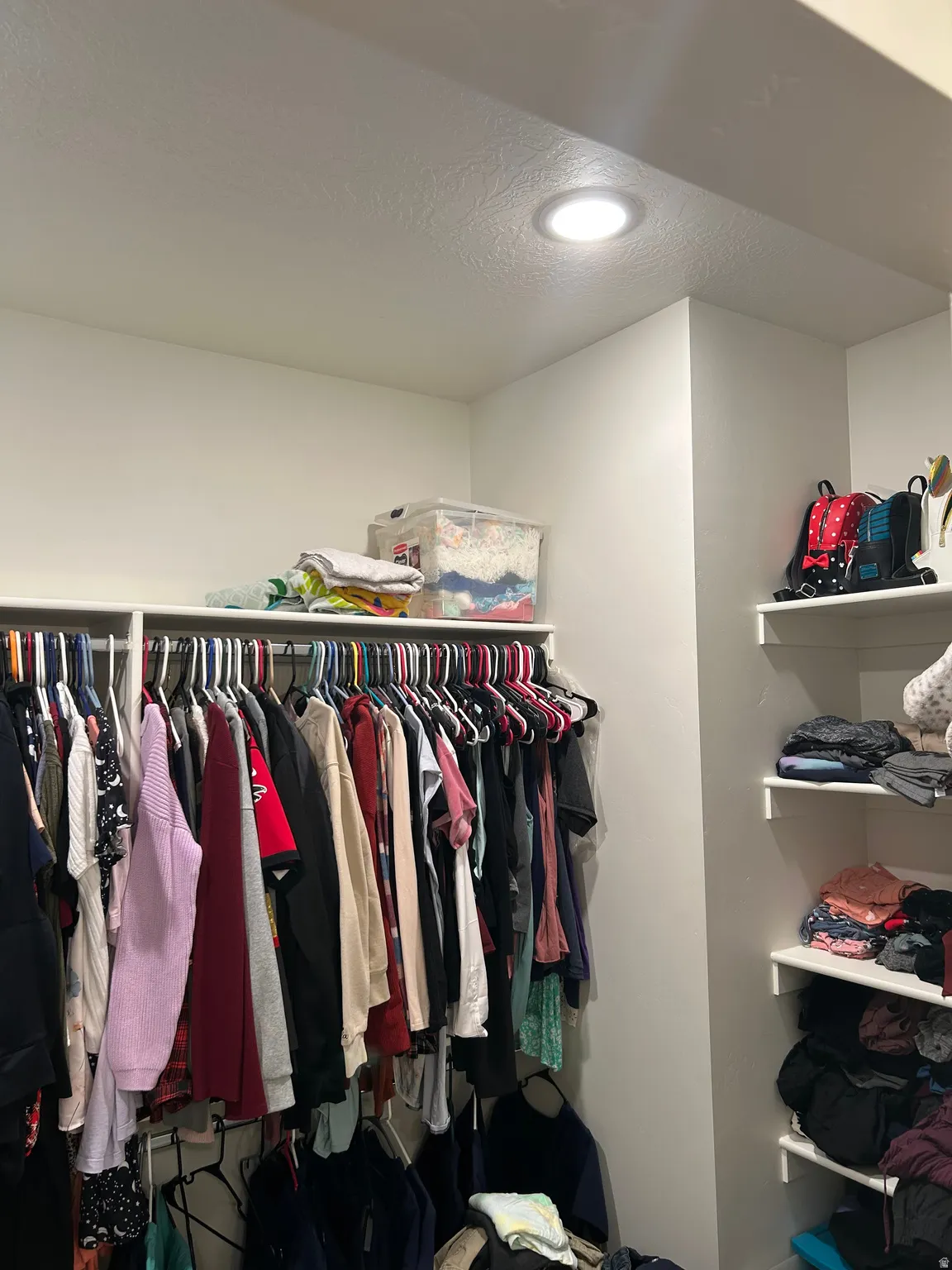 Recessed ceiling lighting illuminates a built-in closet system, featuring multiple hanging rods and shelving units for organized storage