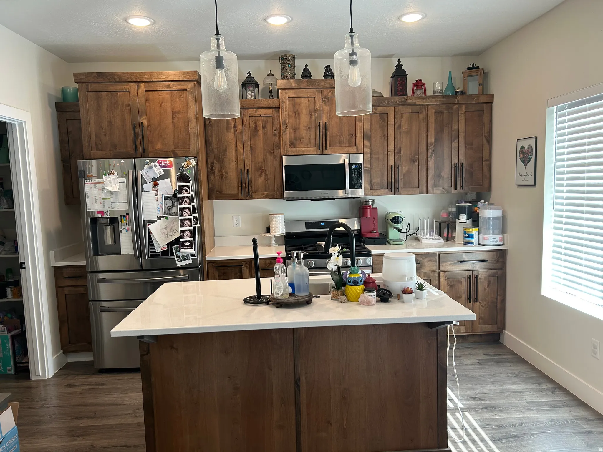 Kitchen featuring a central island with a white countertop, wood-finish cabinetry, stainless steel appliances, pendant lighting, and wood-finish flooring