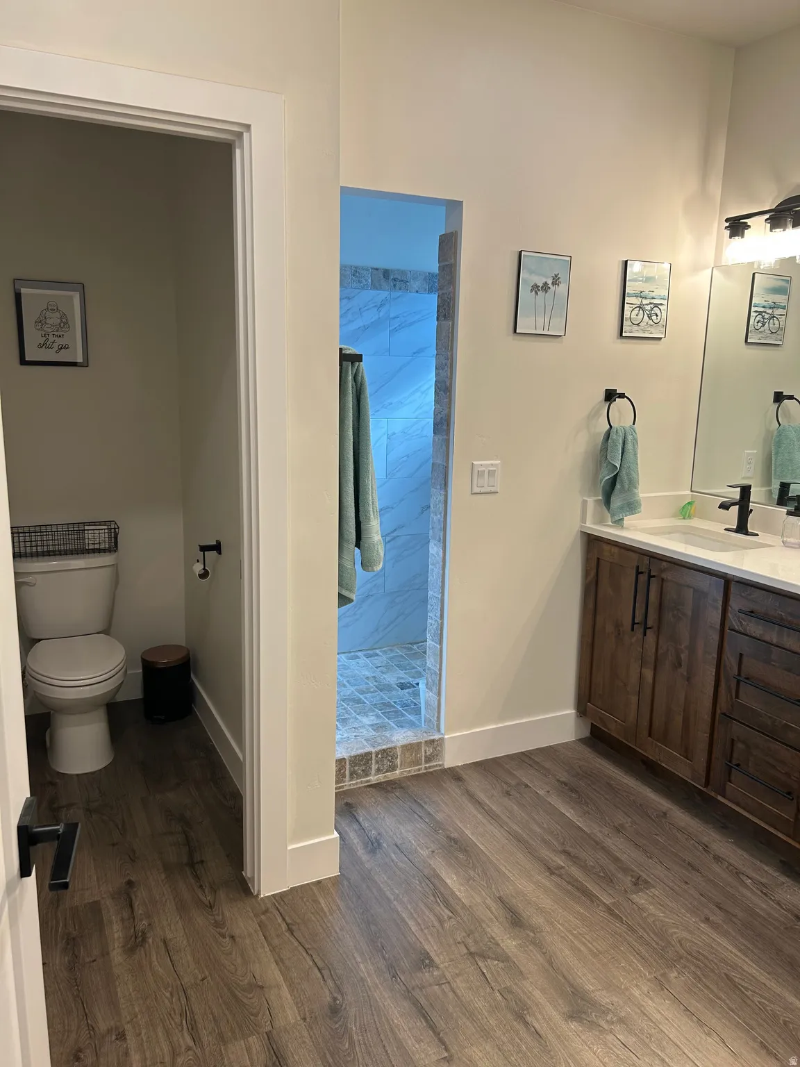 Wood-finish flooring extending into a spacious bathroom featuring a dark wood vanity with a white countertop and dual sinks