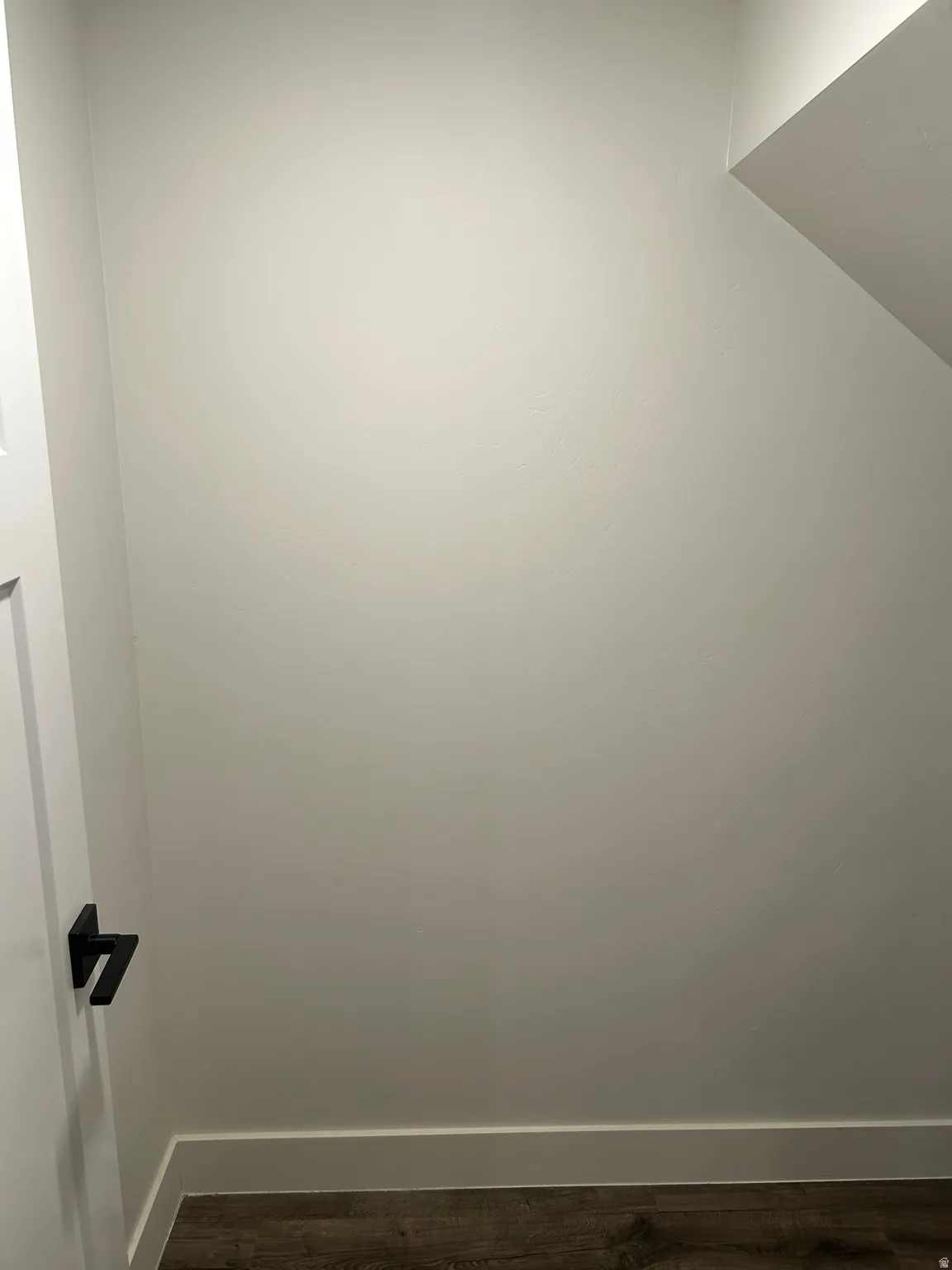 Crisp white walls with a complementary white baseboard, wood-finish flooring, and a modern matte black door handle