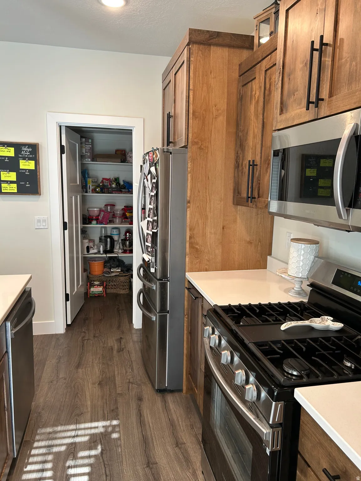 Kitchen featuring wood-finish flooring, stainless steel appliances, light-toned countertops, and wood cabinetry with dark hardware